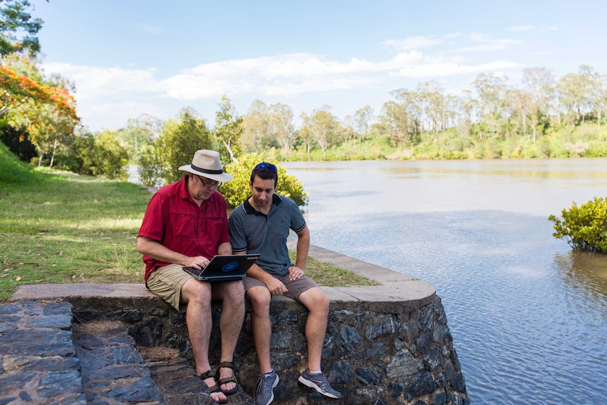 Dr Simon Linke (l) sits with a colleague on the edge of a waterway studying the sounds of fish made in nature.