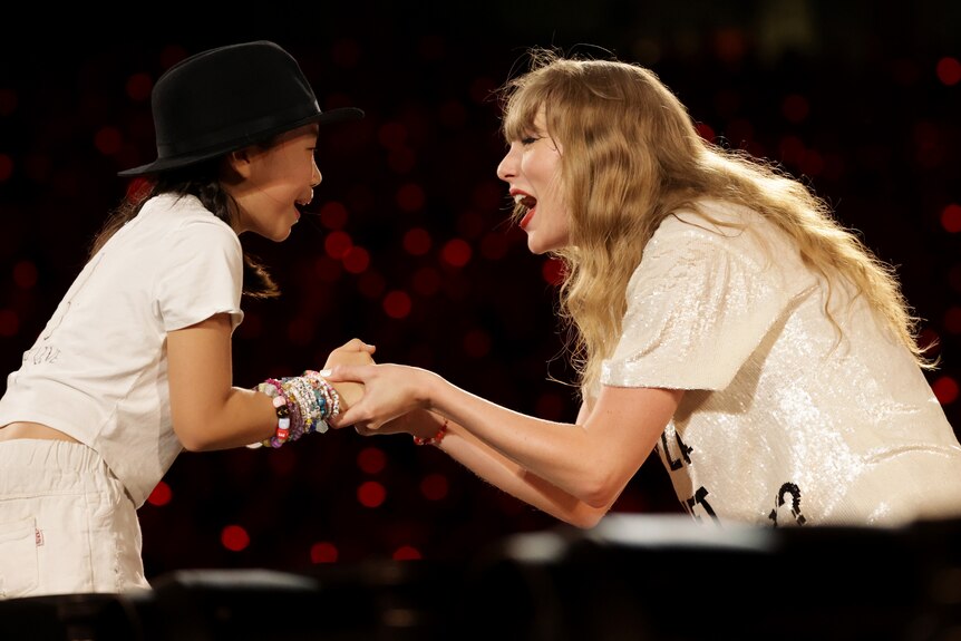 Taylor Swift smiles and clasps the hands of a fan at one of her shows.
