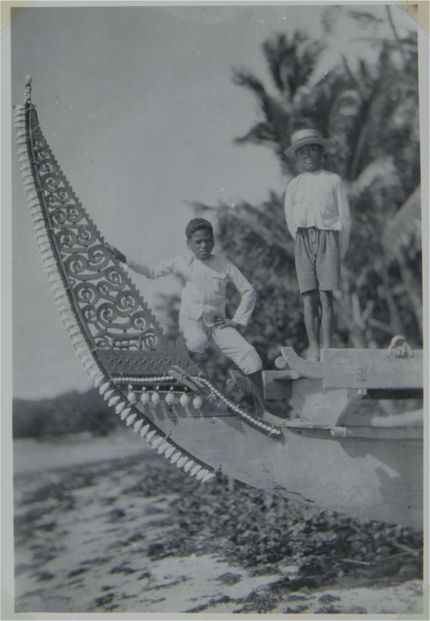 A black and white photo of two young boys on a ship with a decorative laced wood panel on it