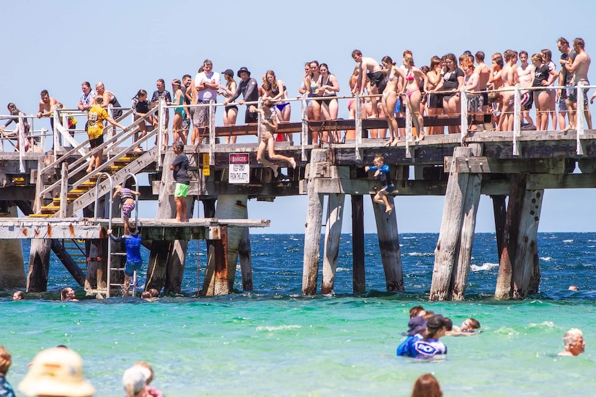 A large group of people line up along the jetty with many others in the water below.