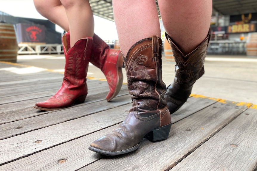 Close up image of two people wearing cowboy boots with their legs crossed at the back.