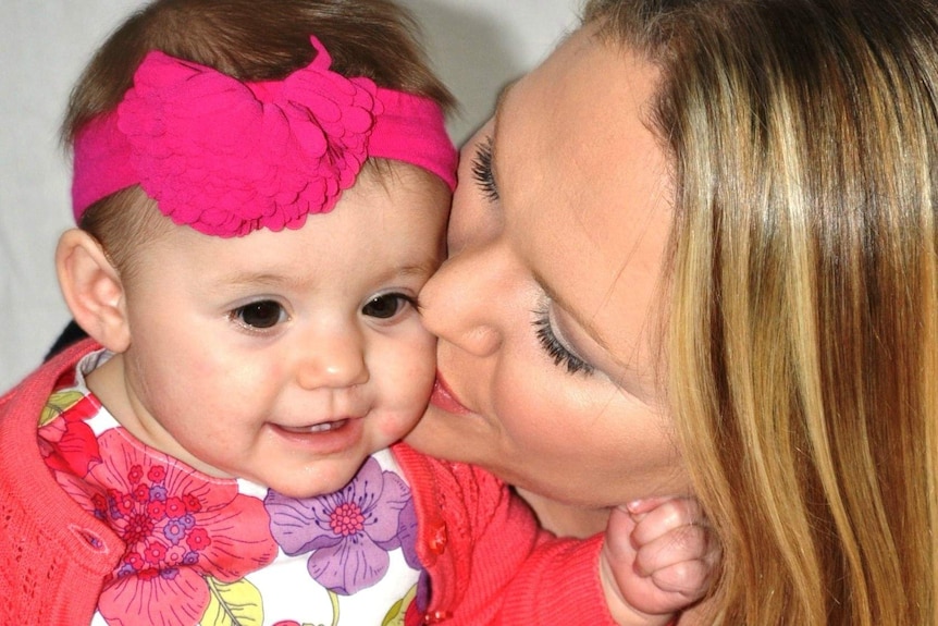 A tight shot of a mother giving her baby daughter a kiss on the cheek