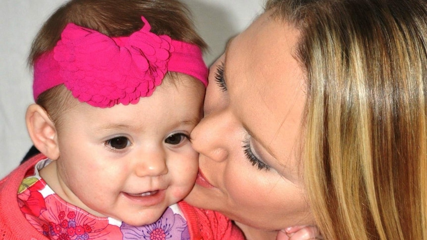 A tight shot of a mother giving her baby daughter a kiss on the cheek