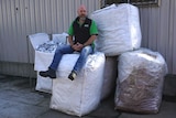 man sitting on a pile of five large bags filled with foil scraps