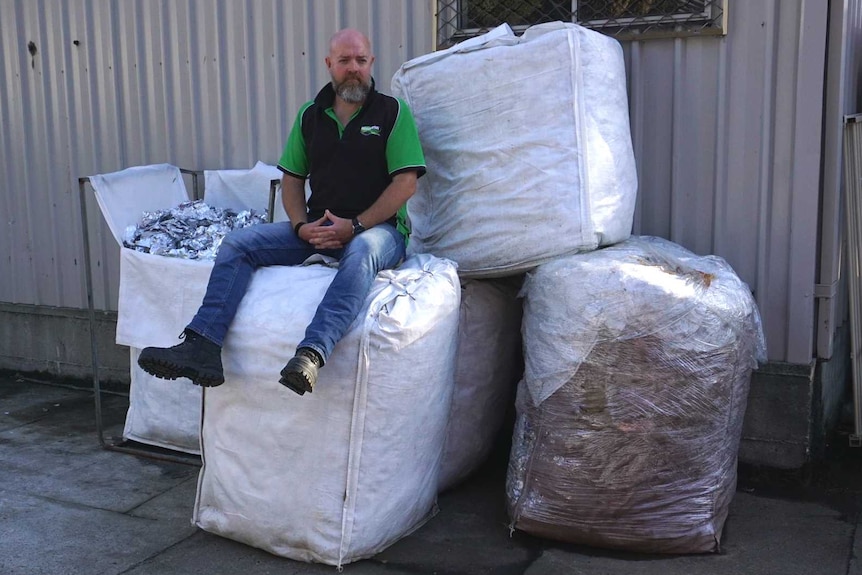 man sitting on a pile of five large bags filled with foil scraps