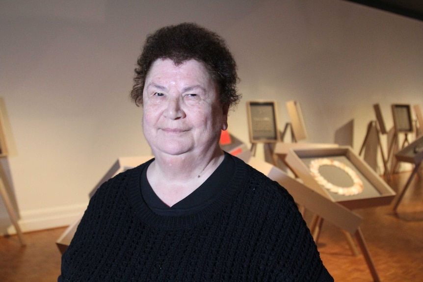 Picture of a woman next to shell necklaces displayed in glass cabinets