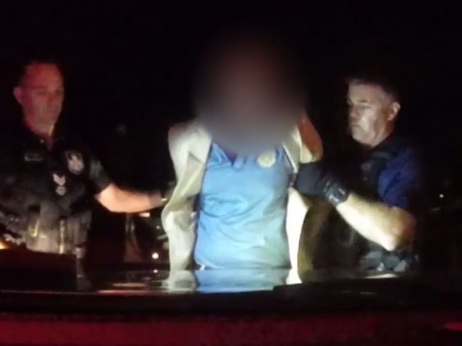 Dashcam vision of two Queensland Police arresting a man at night, he is handcuffed and his face is blurred.