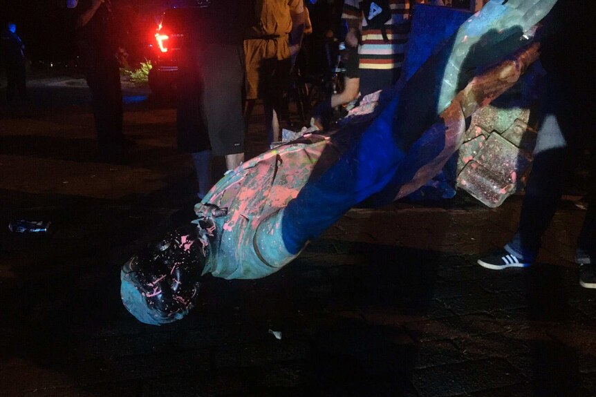 Protesters surround a statue covered in paint at night