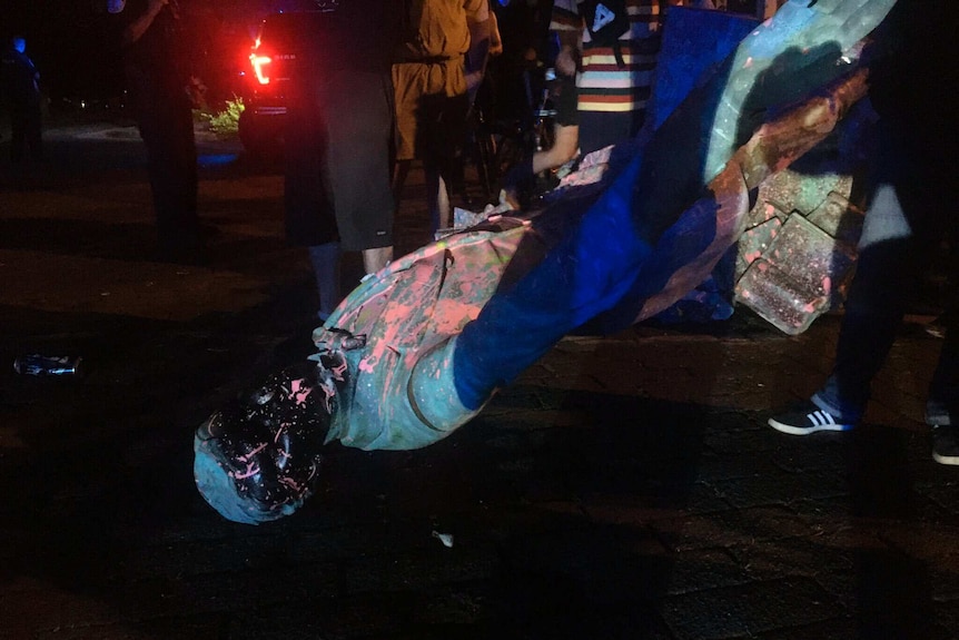 Protesters surround a statue covered in paint at night