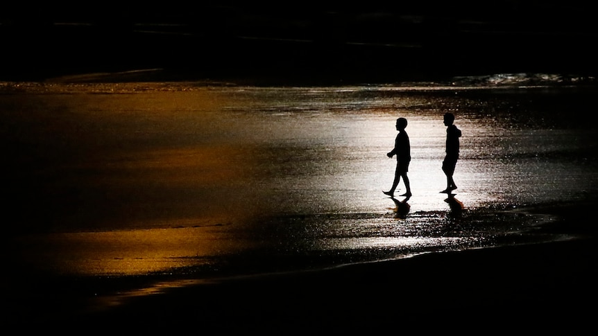 Two boys walk on the beach on a summer's evening.
