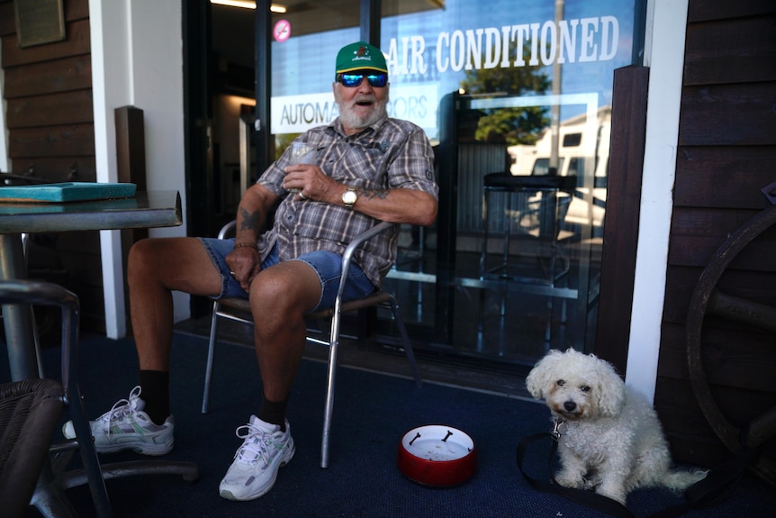 A man drinking a beer sits outside the Lee's Hotel in Ingham with his pet dog sitting quietly on the ground to his right