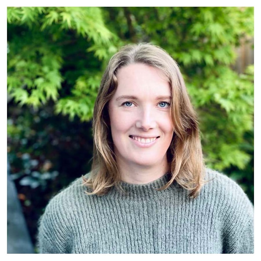 Lizzie Strick with shoulder length brown hair smiling at the camera wearing a green jumper