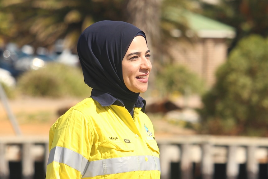 A woman with a head covering stands in hi-vis with water behind her