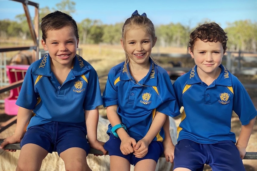 Three kids in school uniform sitting on a fence. 