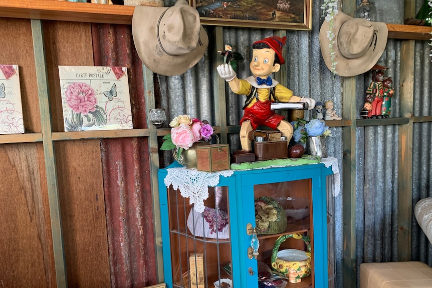 Timber and iron shed filled with colourful nic nacs including a wooden pinocchio doll, vases, flowers, paintings and farm hats