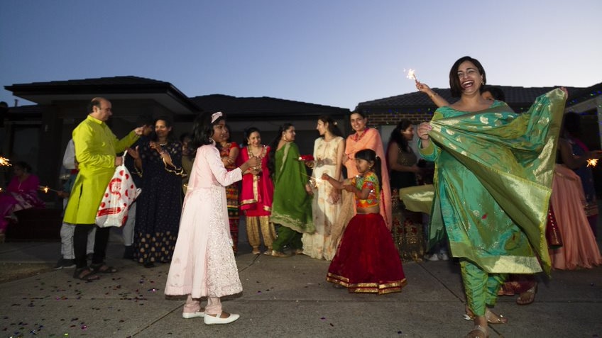 Children with sparklers play as a woman in green Indian dress laughs.