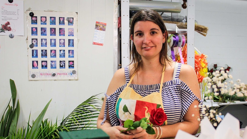 Mount Isa florist Amy Ives standing behind the counter, holding a red rose.