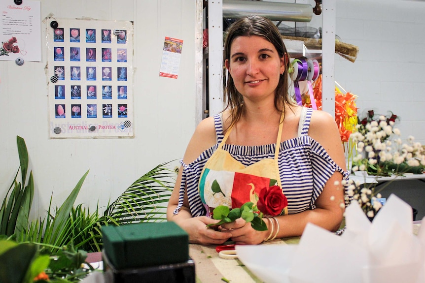 Mount Isa florist Amy Ives standing behind the counter, holding a red rose.