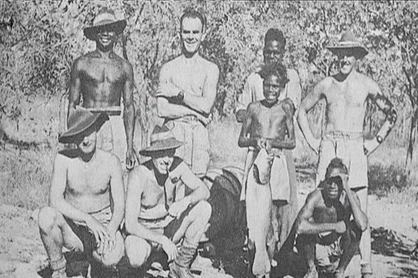 A black and white historical image showing a group of men standing together and smiling in a bush environment.