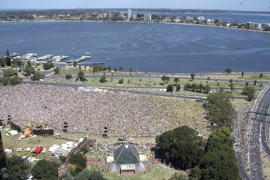 Aerial view of a massive crowd at a park with a river in the background