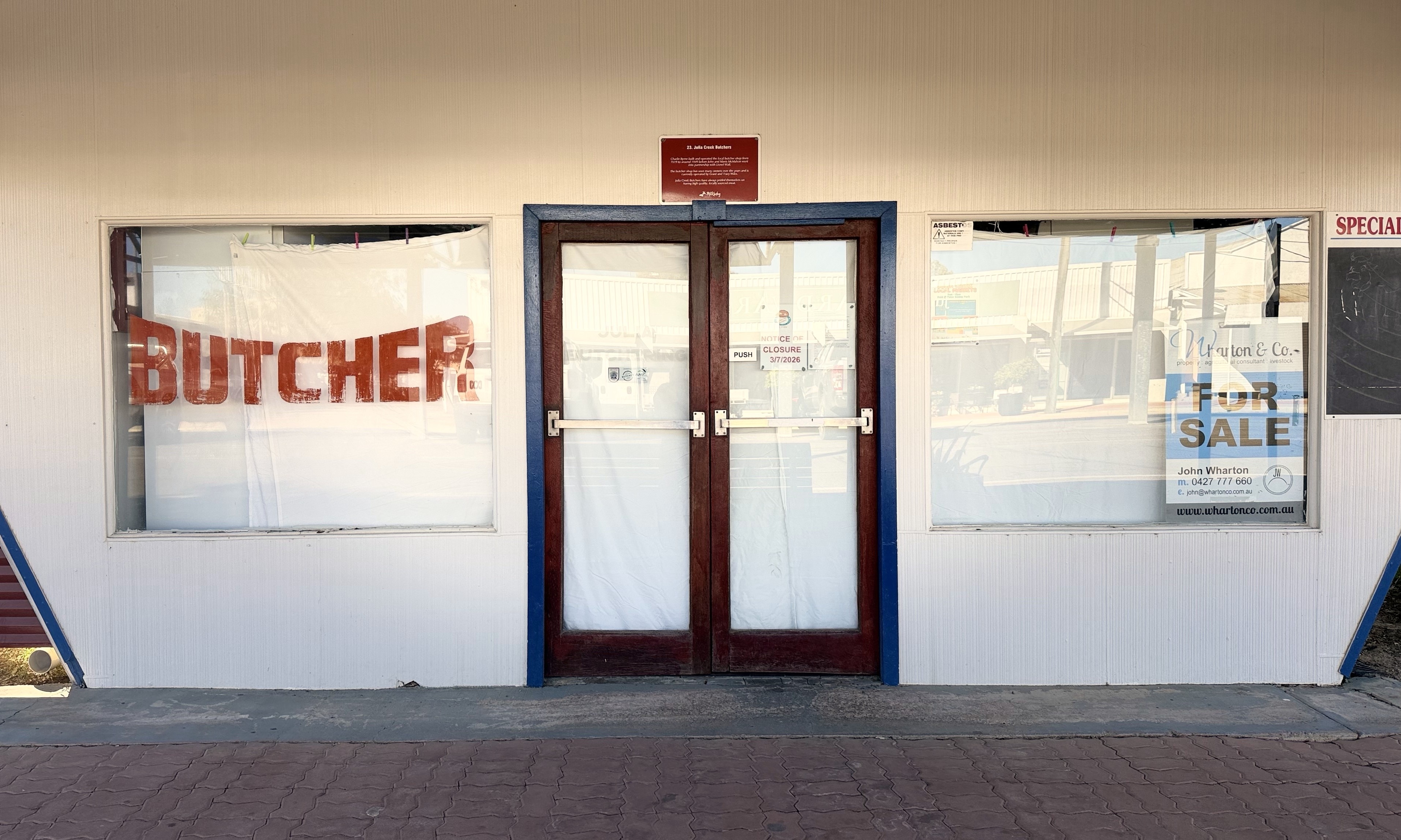 Julia Creek butcher with sheets over windows and for sale sign.