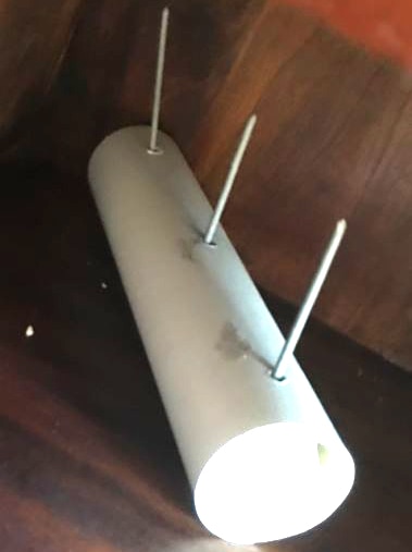A close-up shot of a homemade white pipe bomb, with three sticks protruding from the top, on a wooden shelf.