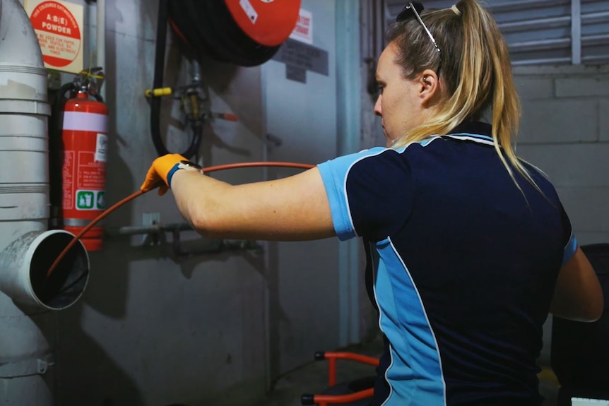 a young woman putting a hose down a pipe to clean