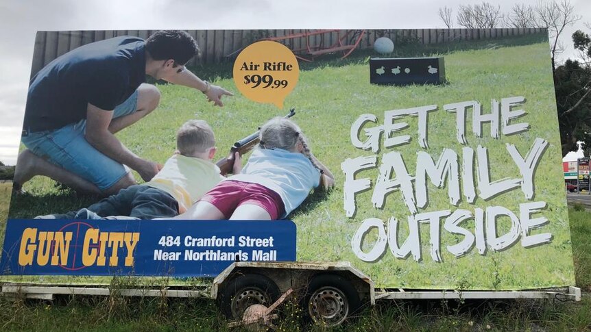 A large advertising billboard depicting a family with young children using air rifles outside