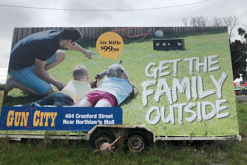 A large advertising billboard depicting a family with young children using air rifles outside