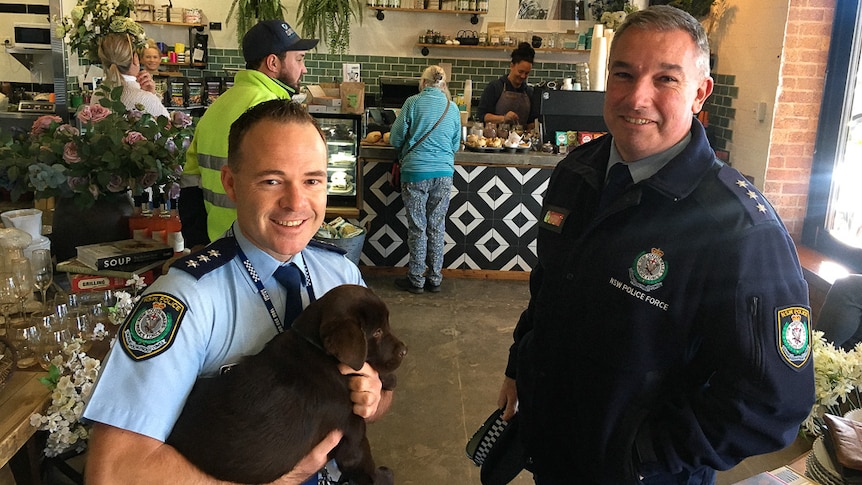 Two police officers, one holding a puppy, stand in a cafe