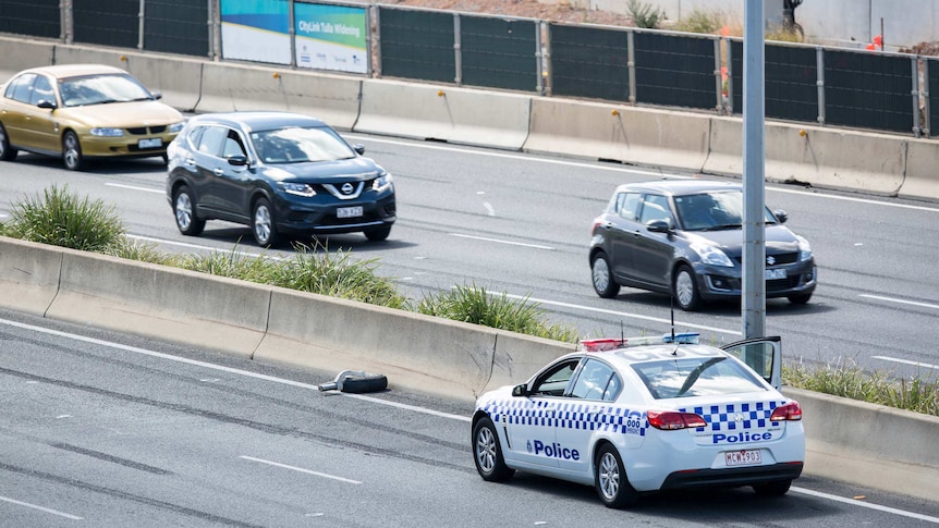 A police car on the Tullamarine Freeway stopped in front of a wheel from a crashed plane.