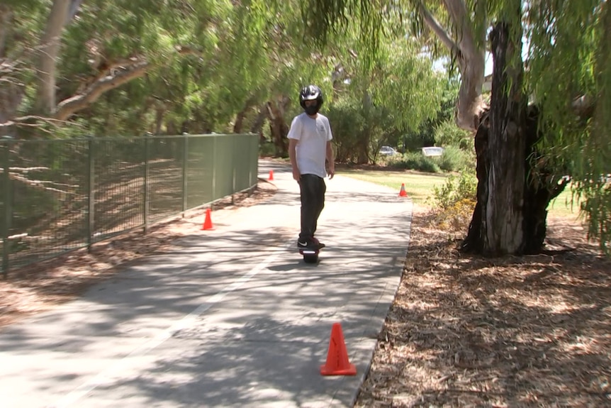 A man rides a one-wheel device on a bike path among trees
