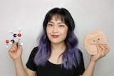 Woman with purple hair holds up science models, in a story about knowing which skinfluencers to trust.