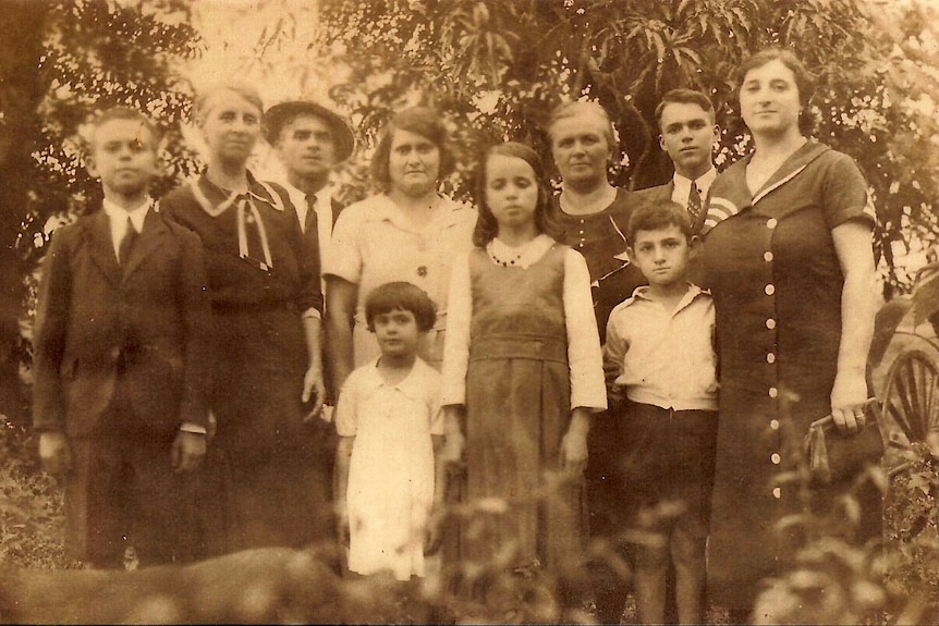 Ten people, adults and children, in a historic black and white photo taken in a garden.