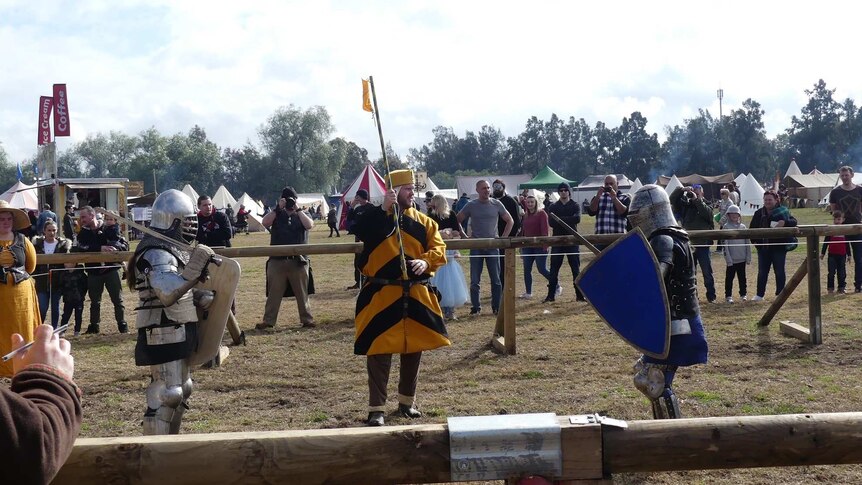 People in medieval costume mock fighting.