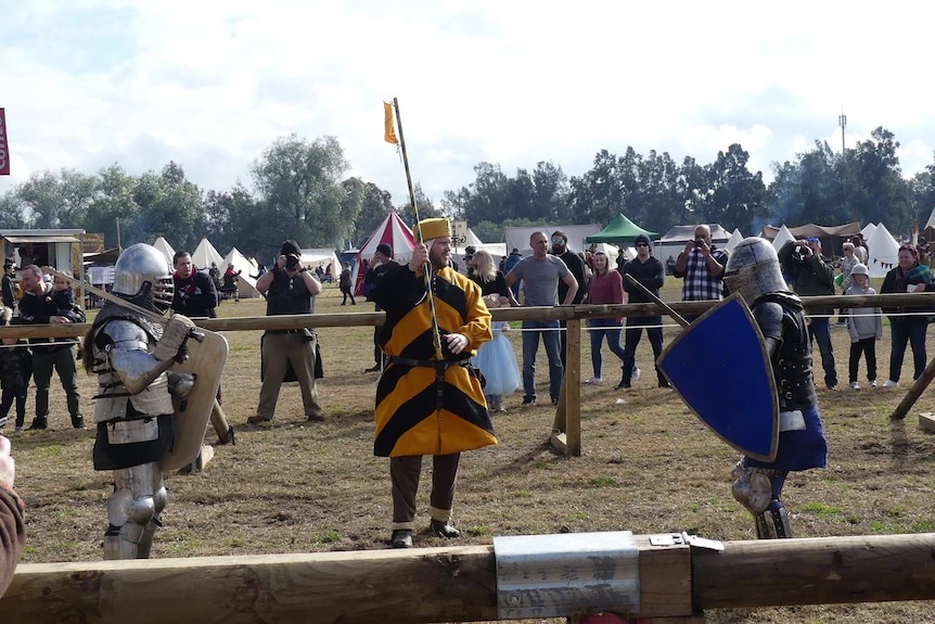 People in medieval costume mock fighting.