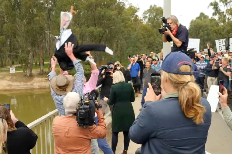 A group of protestors surrounded by press and photographers through an effigy off a bridge and into a river.