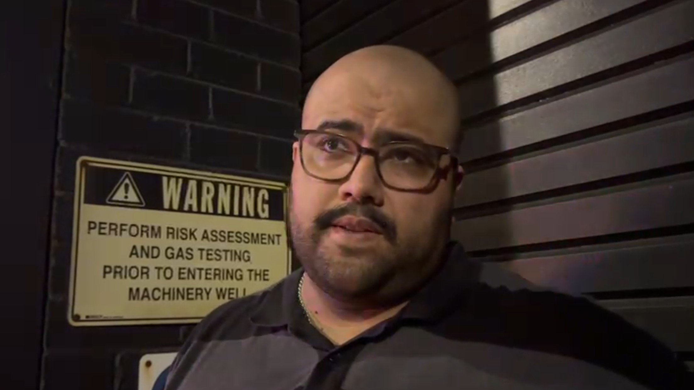 El hombre habla con una persiana detrás, con una señal de advertencia amarilla