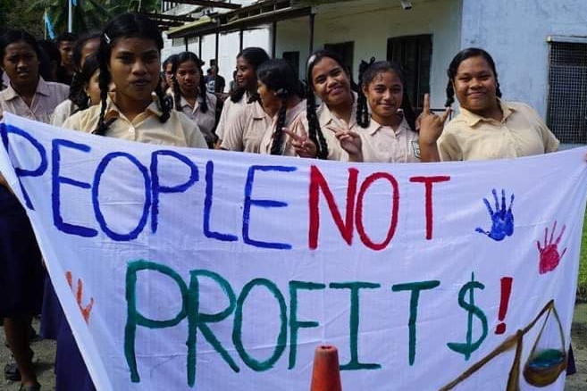 A group of school students in paleyellow shorts hold a sign reading "People not profts!" 