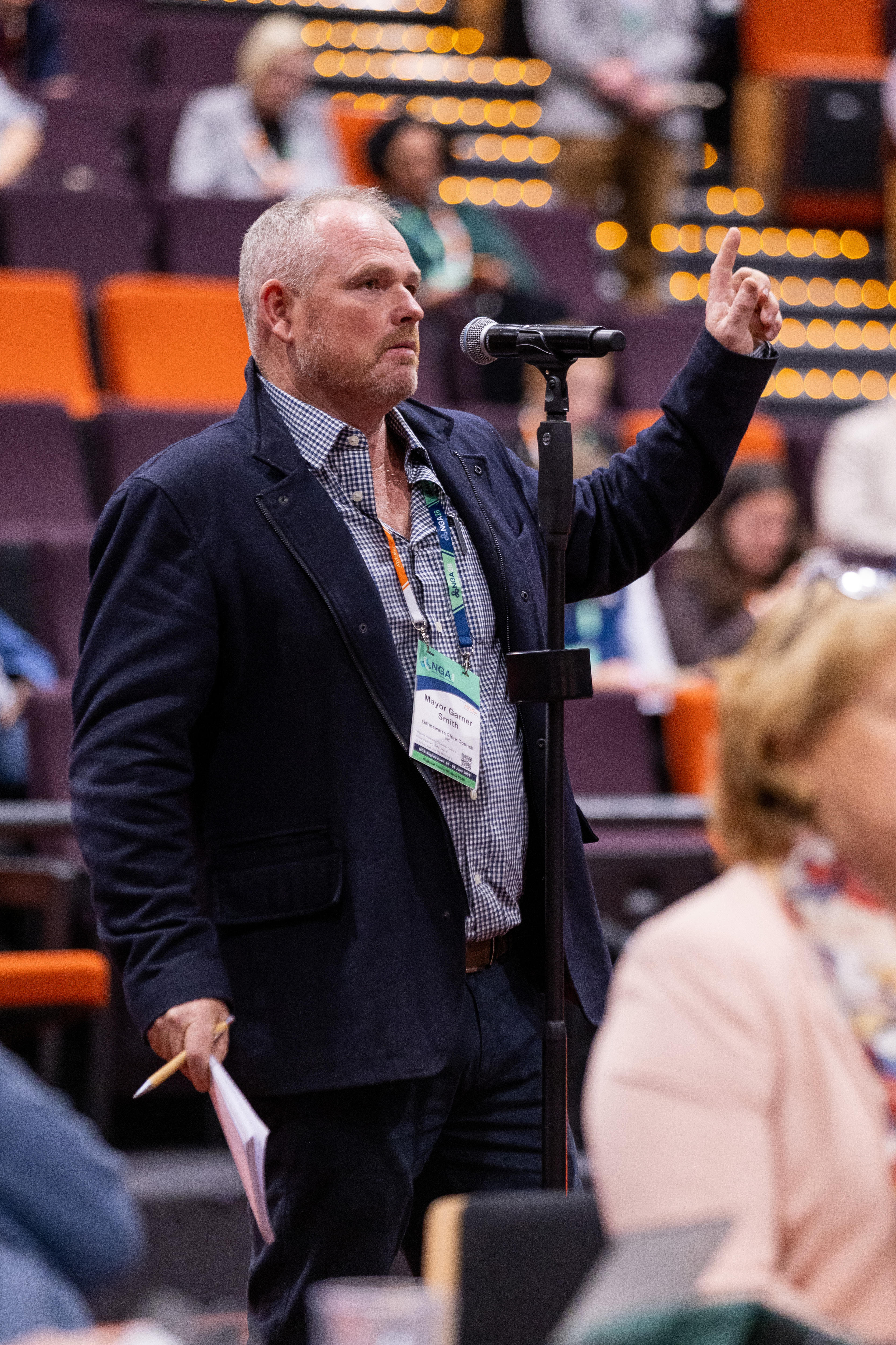 A man standing at a microphone asking a question with his hand raised