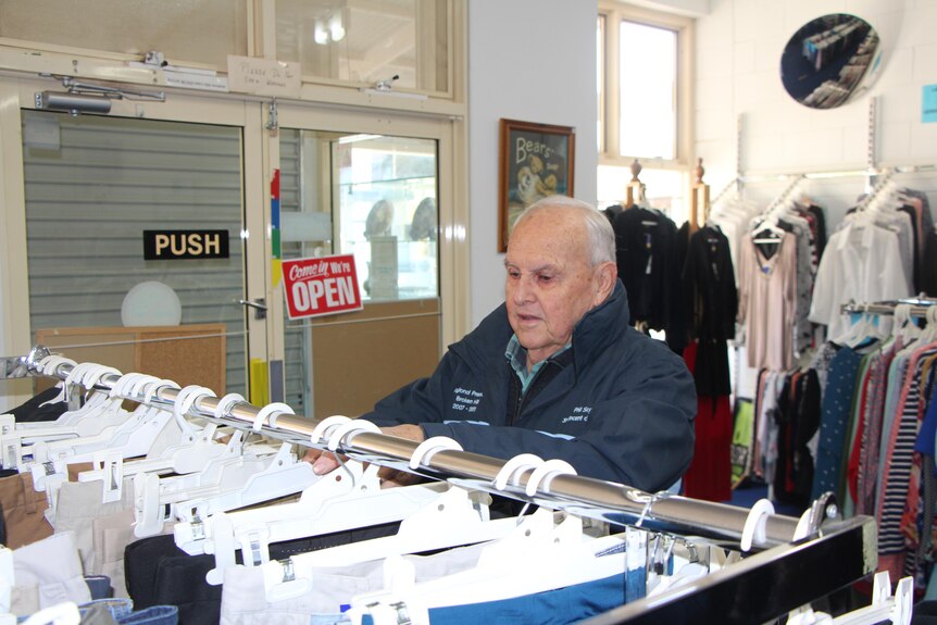 An older man organising clothes on a rack in an op shop.