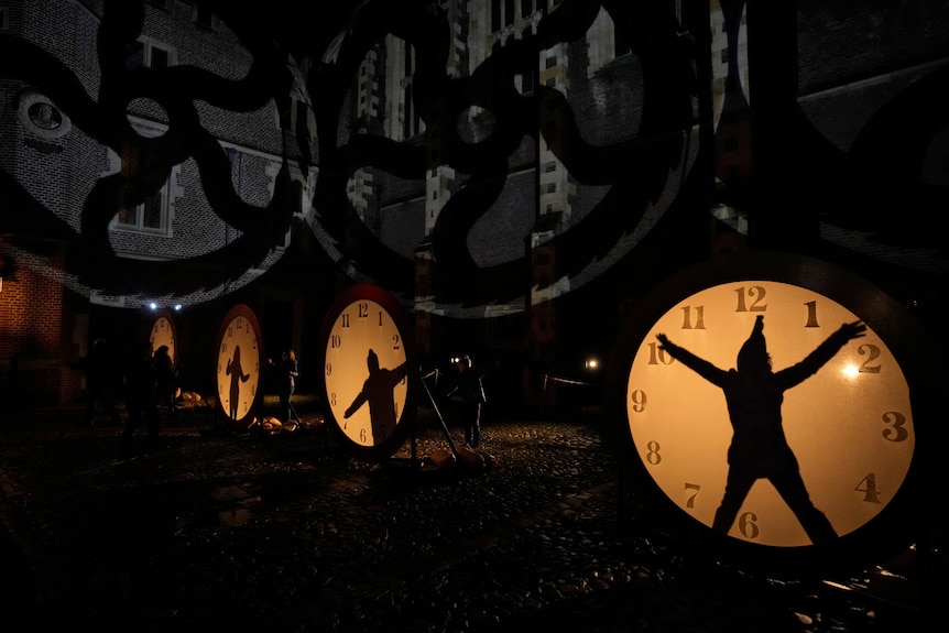 silhouettes of people can be seen on illuminated clock faces near a building in Hampton Court Palace