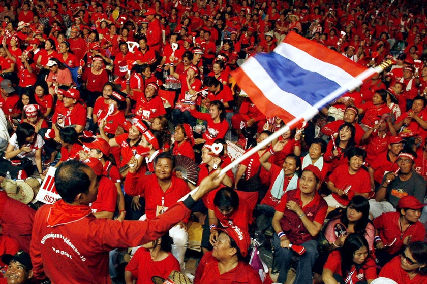A crowd of people wearing red shirts gather to wave Thailand's flag.