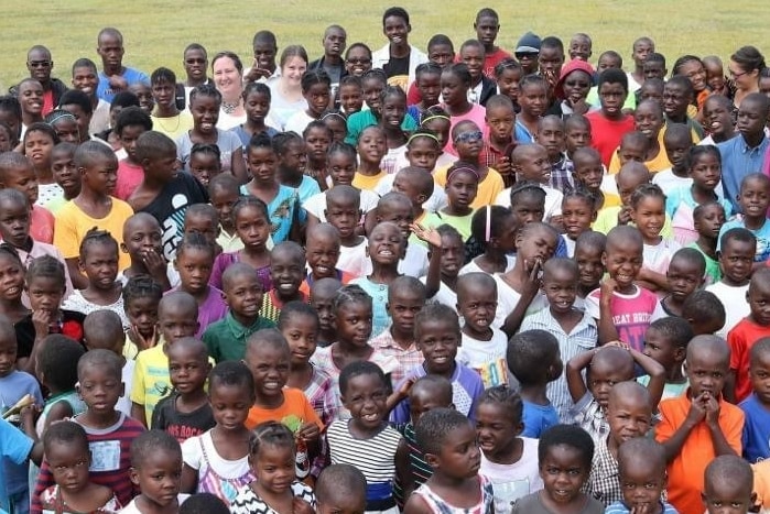 Dozens of young African children in bright clothes with orphanage staff all smiling