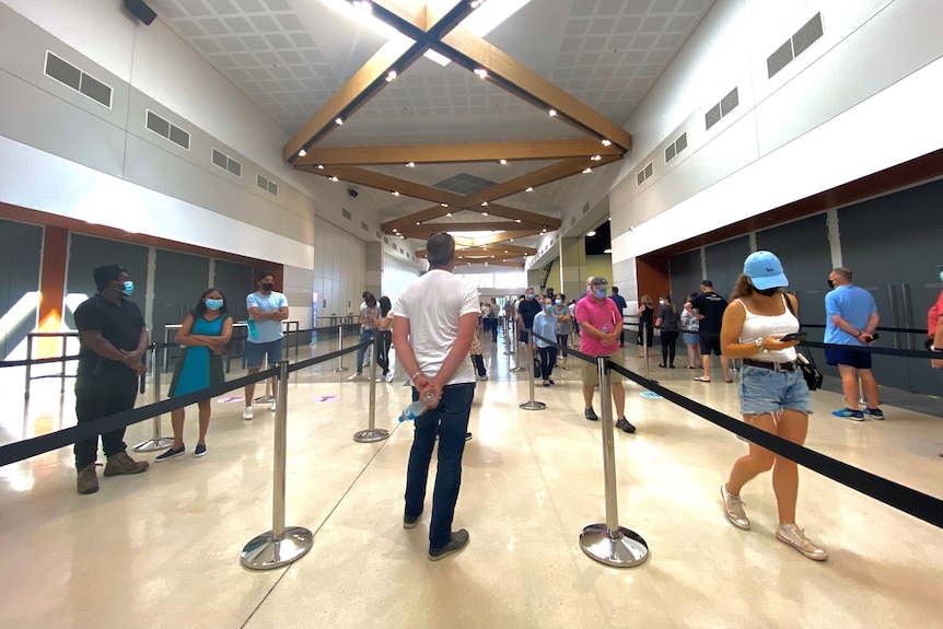 People stand apart in four queues wearing masks inside a building