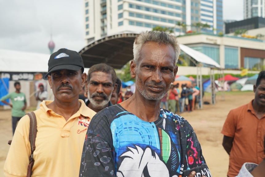 A line of people wearing different coloured shirts stand in a line.