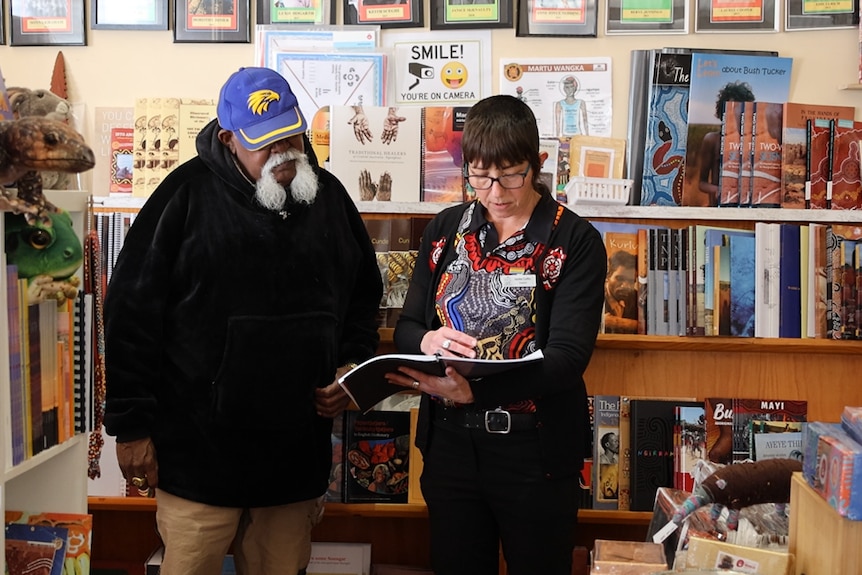 Indigenous man and woman with short hair reading a book.