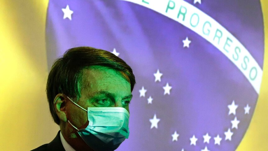 Brazil's President Jair Bolsonaro wears a protective face mask in front of a Brazilian flag.