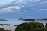 A photo overlooking house roofs, with the ocean, a causeway and an island in the distance