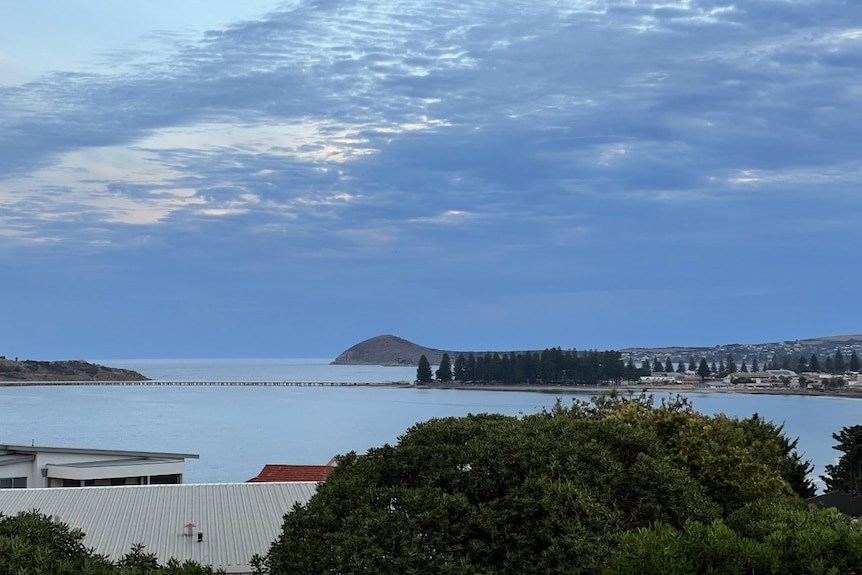 A photo overlooking house roofs, with the ocean, a causeway and an island in the distance